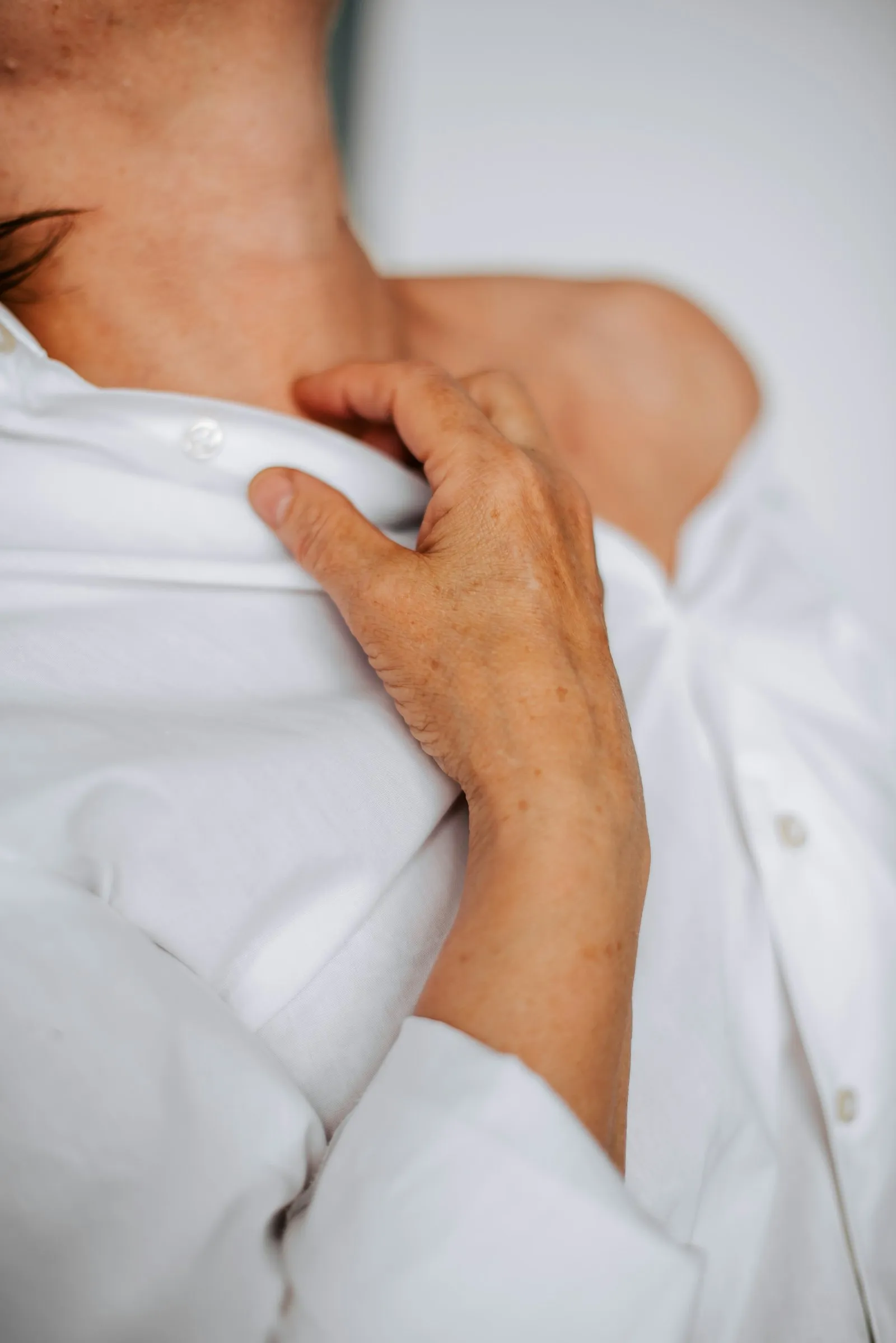 A hand resting gently on the chest over a white shirt