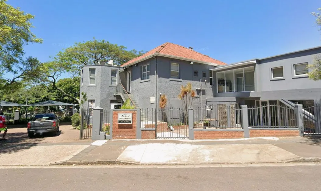 The clinic from Lilian Ngoyi Road: a grey double-storey building with a red tiled roof behind black gates